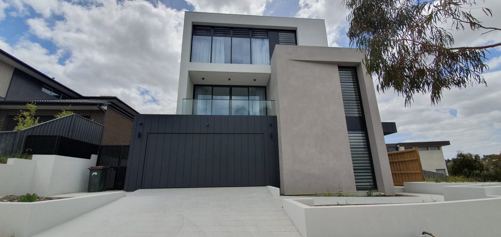 a modern three storey home with a large tilt facade garage door