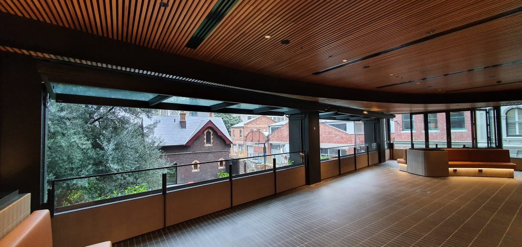 foyer with two large custom tilt windows open overlooking a public space with beautiful trees and a gentle breeze