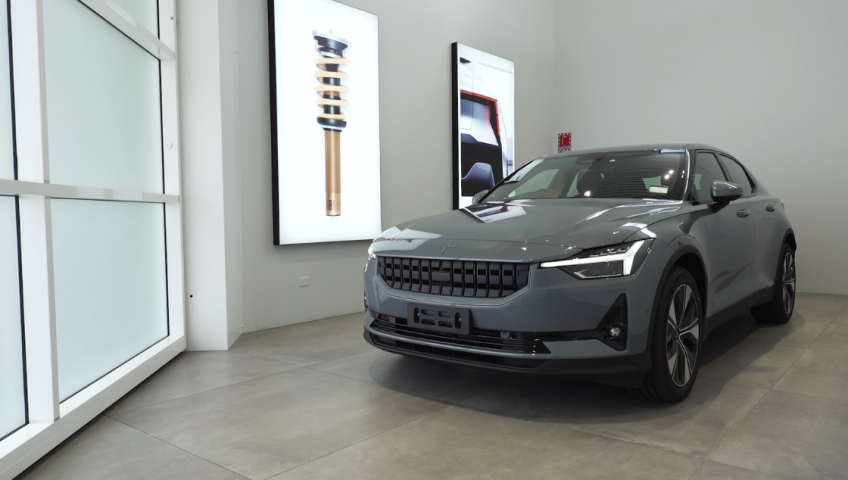 Polestar 2 car in white showroom with closed tilt door, two pictures on wall, and frosted privacy glass