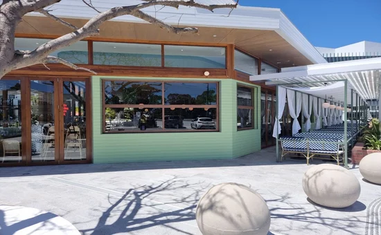 Daytime view of the Spice Market Thai restaurant from an outdoor seating area, showcasing the closed Smartech Folding Windows which complement the green exterior walls and wooden accents under a clear blue sky.