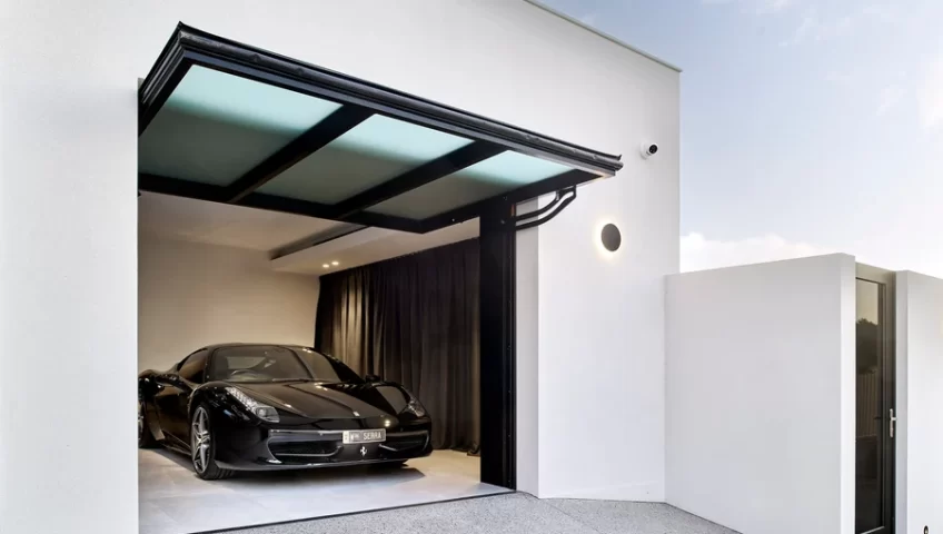 Modern garage with a sleek black car parked inside, featuring a triple-pane glazed tilt wall door in an open position. The door design adds a stylish and functional element to the building's exterior.